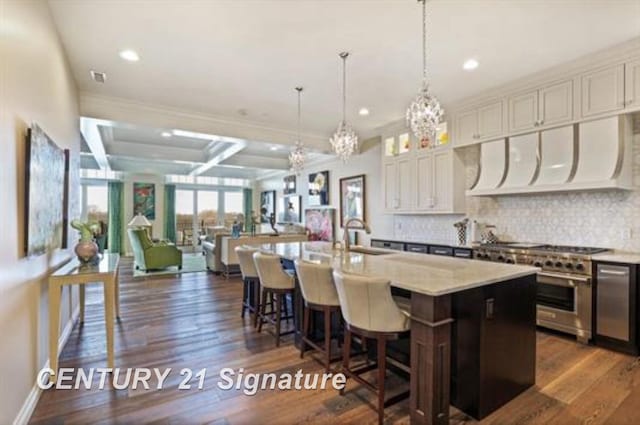 kitchen featuring dark wood-type flooring, a center island with sink, white cabinets, hanging light fixtures, and high end stove