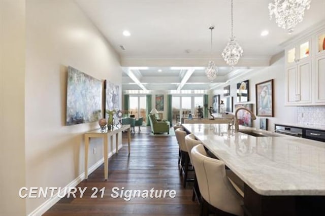 kitchen with white cabinetry, sink, dark wood-type flooring, light stone counters, and pendant lighting