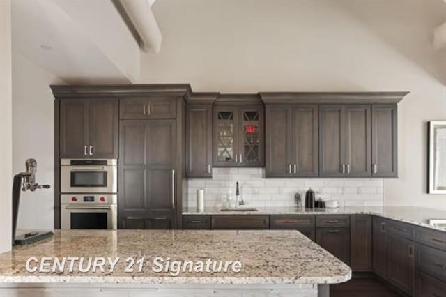 kitchen with dark brown cabinetry, light stone countertops, sink, and stainless steel double oven