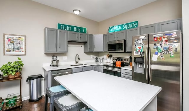 kitchen featuring a breakfast bar, gray cabinetry, a sink, appliances with stainless steel finishes, and light countertops