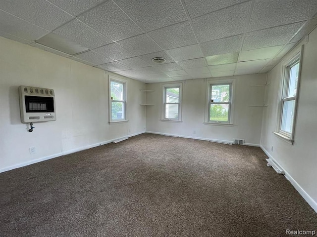 carpeted empty room featuring heating unit and a paneled ceiling