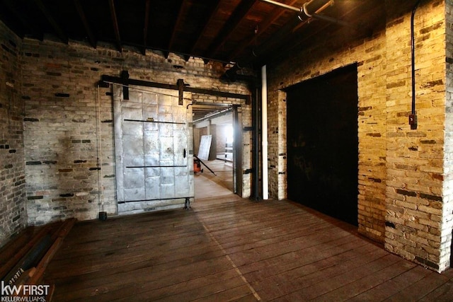 unfurnished room featuring wood-type flooring, a barn door, and brick wall