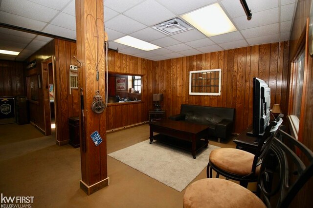 carpeted living room featuring a paneled ceiling and wooden walls