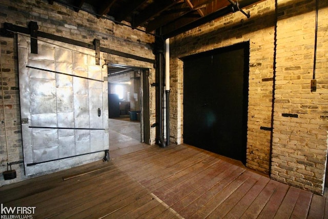 interior space with a barn door, brick wall, and hardwood / wood-style flooring