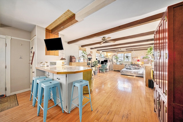 kitchen featuring a kitchen bar, kitchen peninsula, light wood-type flooring, beamed ceiling, and tile counters