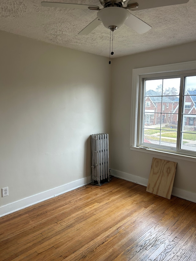 spare room with radiator heating unit, a textured ceiling, light hardwood / wood-style flooring, and ceiling fan