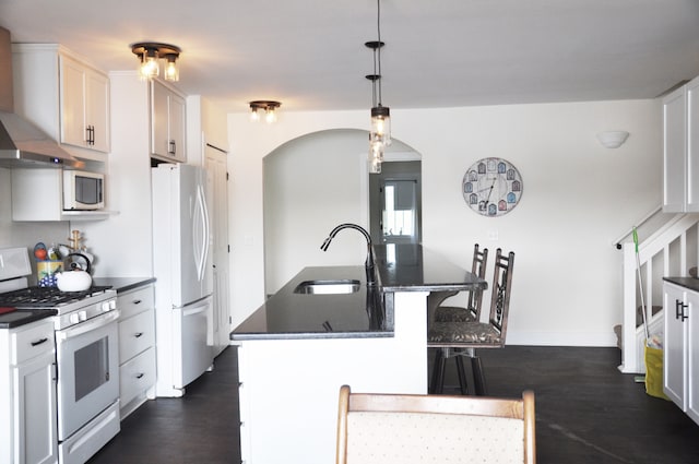 kitchen with wall chimney range hood, white gas range oven, dark hardwood / wood-style floors, stainless steel fridge, and white cabinetry