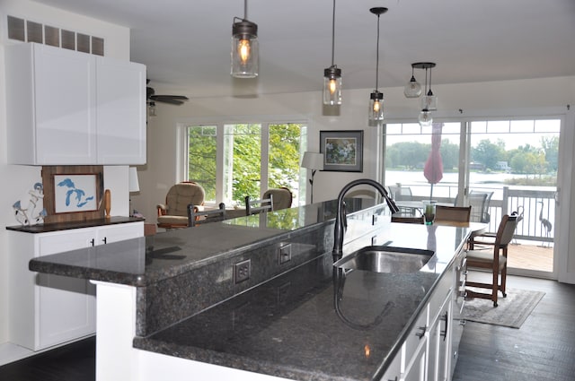 kitchen with dark stone counters, dark wood-type flooring, sink, white cabinetry, and a large island