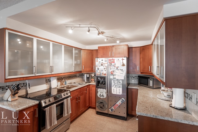 kitchen featuring sink, rail lighting, light stone counters, backsplash, and appliances with stainless steel finishes