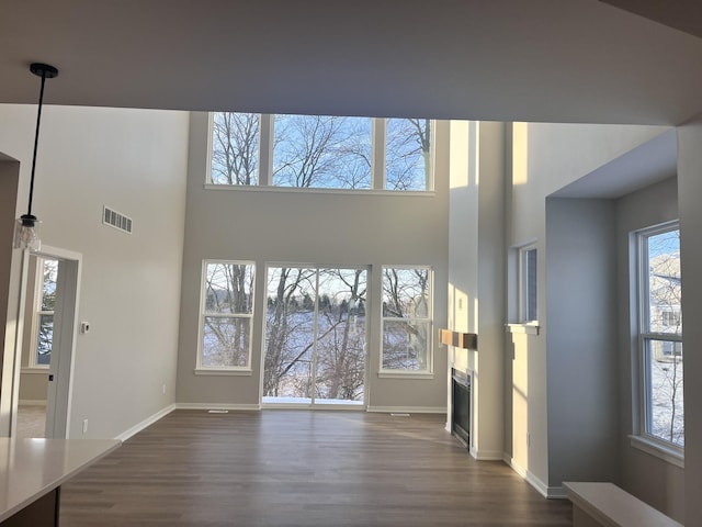 unfurnished living room featuring a glass covered fireplace, dark wood finished floors, visible vents, and baseboards