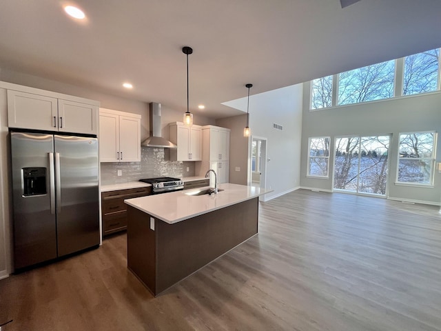 kitchen with a sink, white cabinetry, appliances with stainless steel finishes, decorative backsplash, and wall chimney exhaust hood