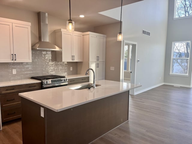 kitchen with visible vents, a sink, wall chimney range hood, backsplash, and gas stove