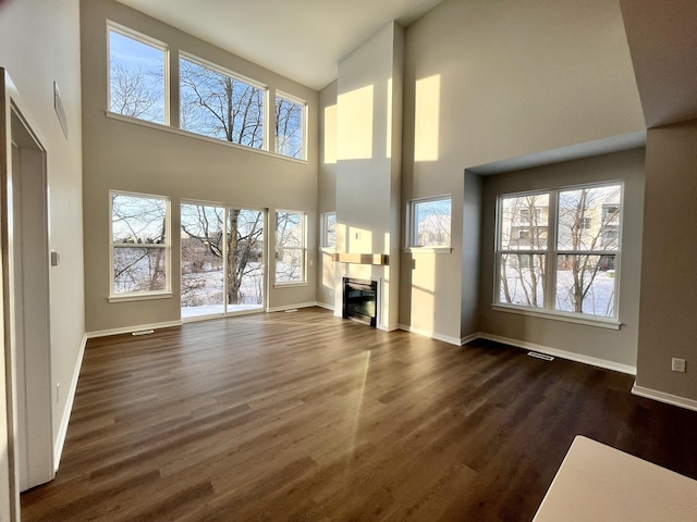 unfurnished living room with dark wood-style floors, a glass covered fireplace, a healthy amount of sunlight, and baseboards