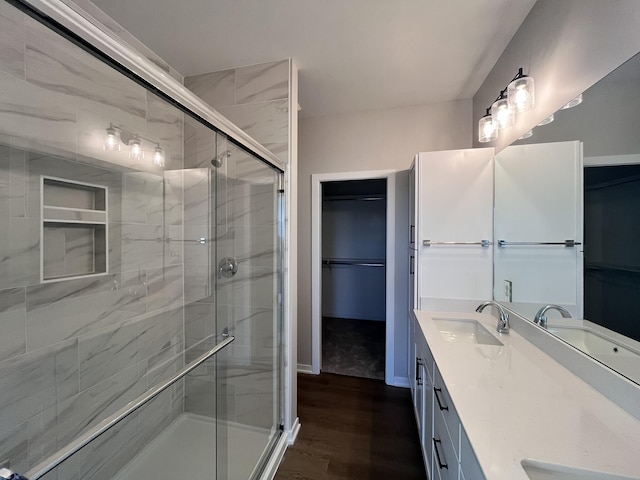 bathroom featuring a walk in closet, a sink, a shower stall, and wood finished floors