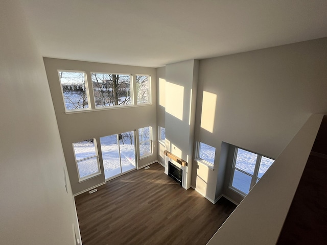 unfurnished living room with baseboards, visible vents, a towering ceiling, dark wood-type flooring, and a fireplace