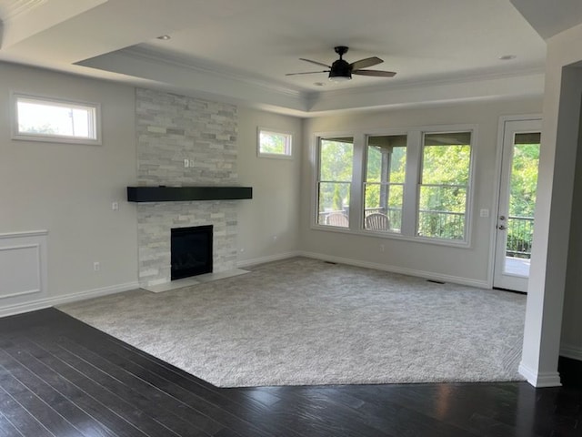 unfurnished living room with ornamental molding, a tray ceiling, ceiling fan, dark wood-type flooring, and a fireplace