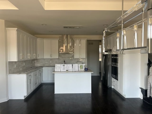 kitchen with pendant lighting, stainless steel appliances, white cabinetry, and wall chimney exhaust hood