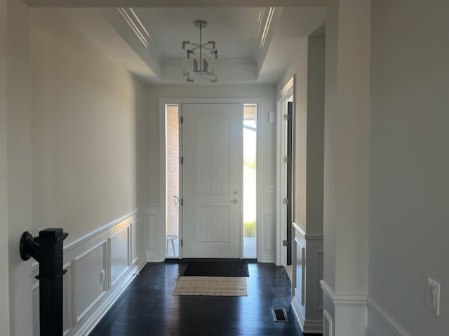 entrance foyer with dark hardwood / wood-style flooring, a tray ceiling, an inviting chandelier, and crown molding