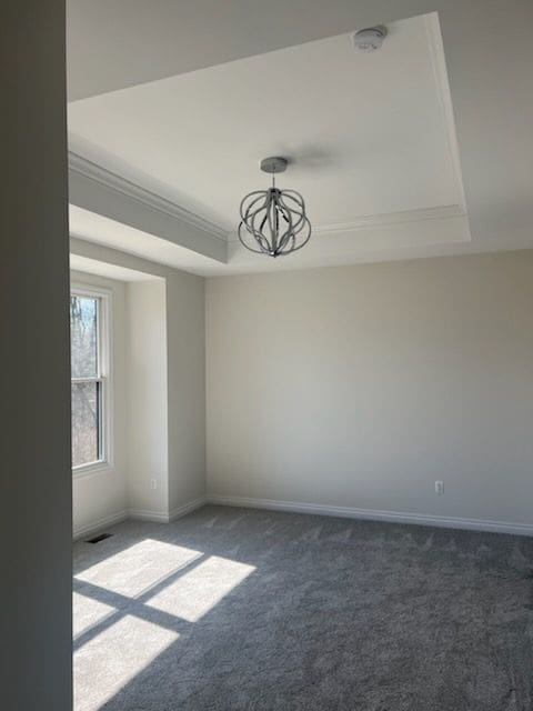 empty room featuring a tray ceiling, crown molding, a notable chandelier, and dark colored carpet