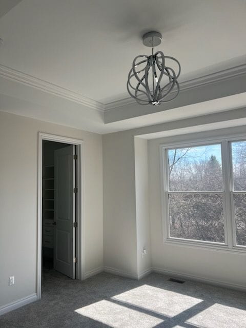 carpeted empty room with a notable chandelier and crown molding