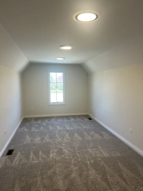 bonus room with dark colored carpet and vaulted ceiling