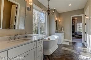 bathroom featuring vanity, parquet flooring, a tub to relax in, and a chandelier