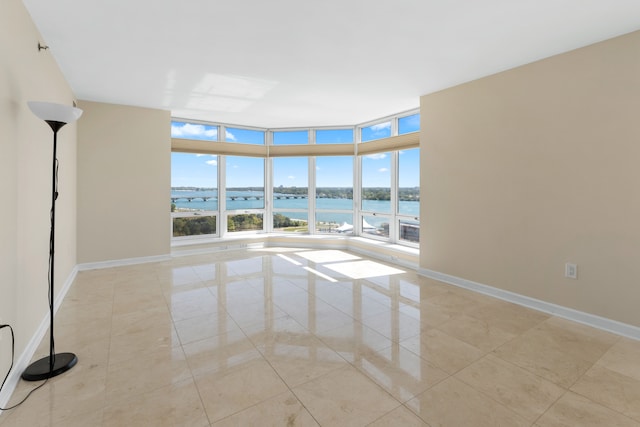 unfurnished room with expansive windows, a water view, and light tile patterned floors