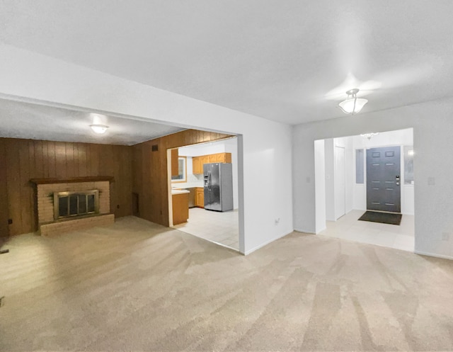 unfurnished living room featuring a fireplace, light colored carpet, and wood walls