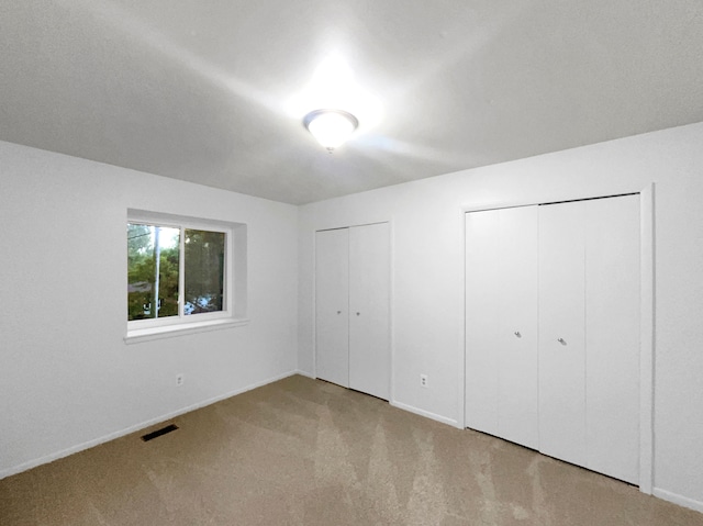 unfurnished bedroom with light carpet and two closets