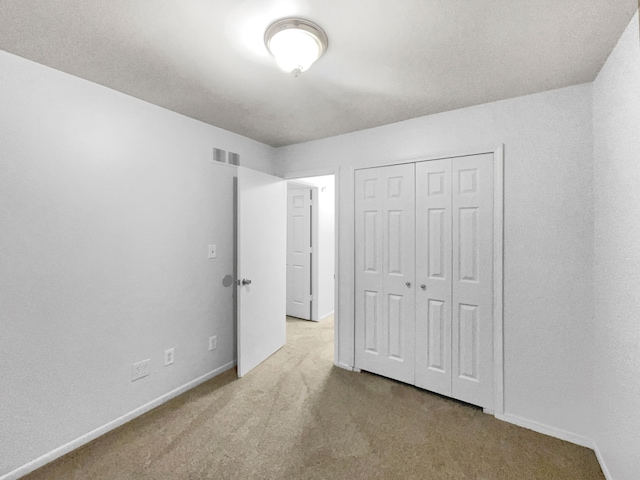 unfurnished bedroom with light colored carpet and a closet