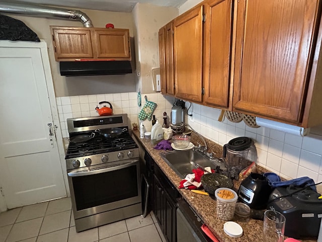 kitchen featuring stainless steel gas range oven, backsplash, dark stone counters, sink, and light tile patterned floors