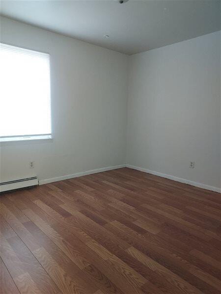 empty room featuring dark hardwood / wood-style floors and a baseboard heating unit