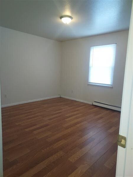 unfurnished room featuring dark hardwood / wood-style flooring and a baseboard radiator