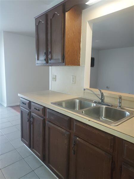 kitchen with dark brown cabinetry, light tile patterned floors, and sink