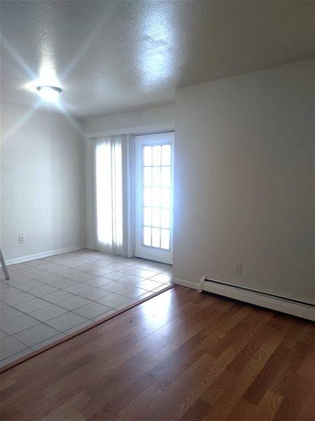 empty room featuring wood-type flooring, a textured ceiling, and a baseboard heating unit