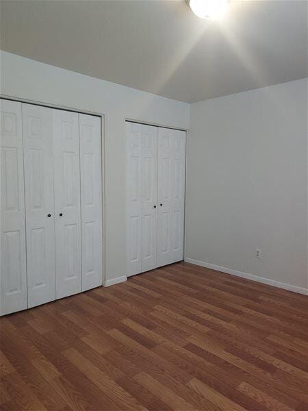 unfurnished bedroom featuring dark hardwood / wood-style flooring and two closets