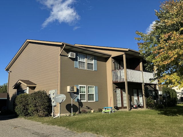 back of property with a lawn, a balcony, and an AC wall unit