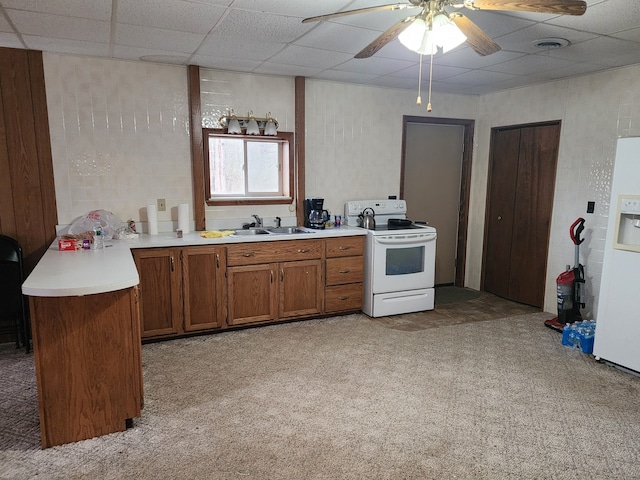 kitchen with a paneled ceiling, white appliances, ceiling fan, light colored carpet, and kitchen peninsula