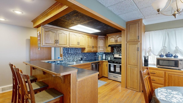 kitchen with kitchen peninsula, stainless steel appliances, a notable chandelier, and light hardwood / wood-style floors