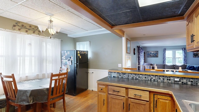 kitchen with black fridge, light hardwood / wood-style flooring, a chandelier, a paneled ceiling, and ornamental molding