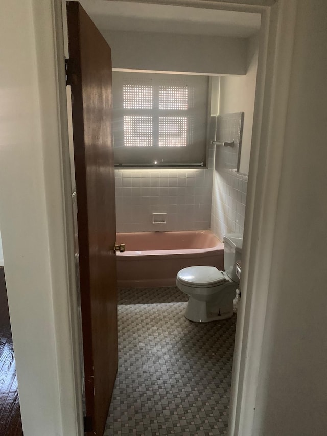 bathroom with tile patterned floors, toilet, tile walls, and a tub