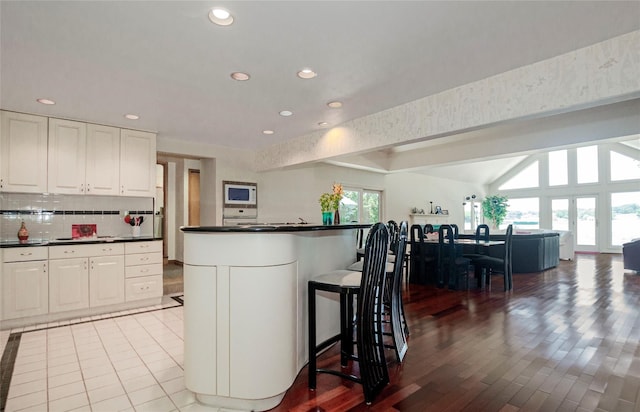 kitchen with white microwave, white cabinets, a kitchen breakfast bar, decorative backsplash, and light wood-type flooring