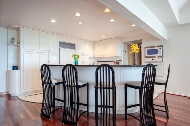 kitchen with a kitchen breakfast bar, white cabinetry, dark hardwood / wood-style floors, and white appliances