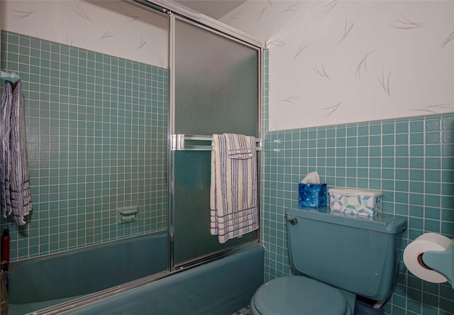 bathroom featuring bath / shower combo with glass door, tile walls, and toilet