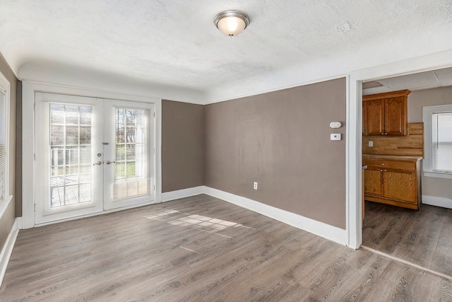 empty room with a textured ceiling, light hardwood / wood-style flooring, and french doors