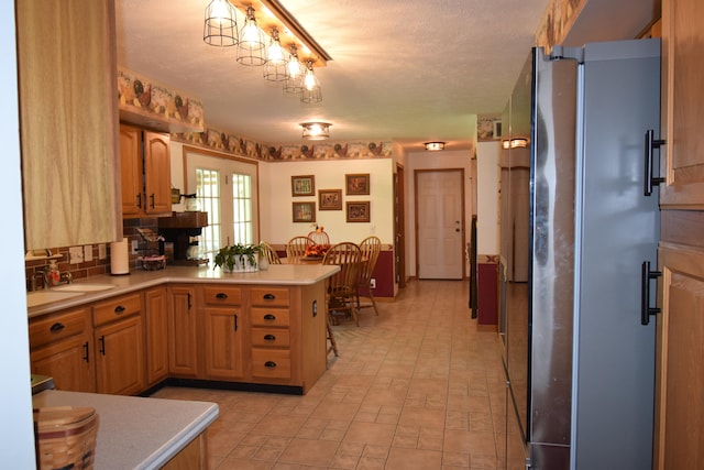 kitchen featuring stainless steel refrigerator, sink, tasteful backsplash, kitchen peninsula, and a textured ceiling