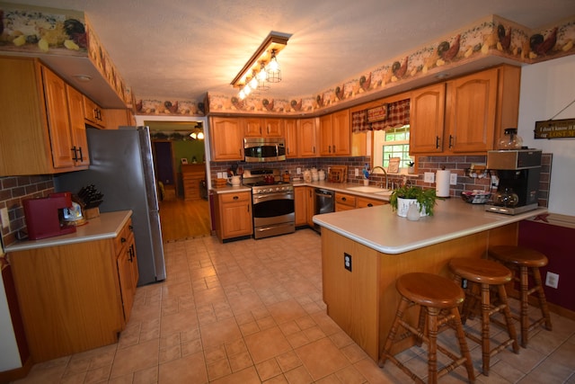 kitchen with track lighting, sink, decorative backsplash, appliances with stainless steel finishes, and kitchen peninsula