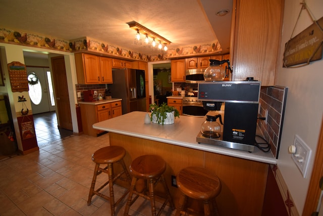 kitchen featuring kitchen peninsula, appliances with stainless steel finishes, rail lighting, decorative backsplash, and a kitchen breakfast bar