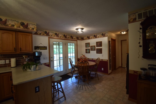 kitchen with french doors, a textured ceiling, tasteful backsplash, and a breakfast bar area