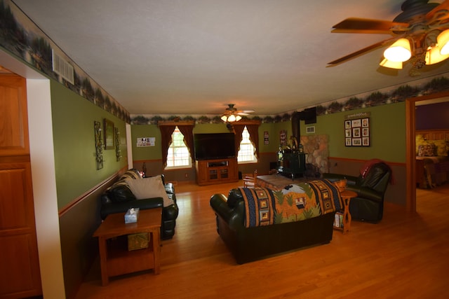 living room with a wood stove, ceiling fan, and light hardwood / wood-style floors